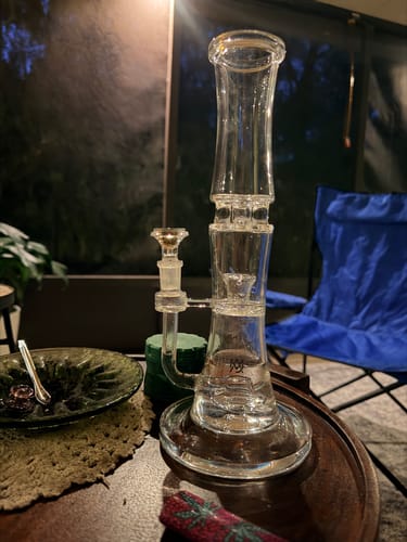 Reviewer's MJ Arsenal Spire Glass Water Pipe filled with smoke on a table during an evening session.
