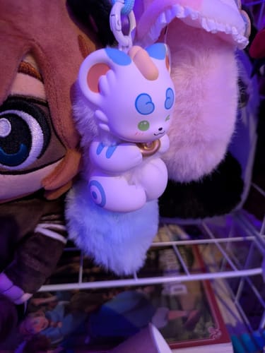Reviewer's Fabulous Beasts plush pendant, a cute white and blue creature with a fluffy tail, hanging among other plush toys.