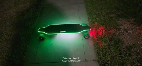 Reviewer's skateboard with green Meepo Cyclone wheels, shown at night with bright green underglow and red taillights.
