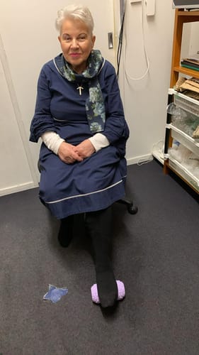 Customer seated in a chair, using the purple Vibit ROLL to massage the sole of her foot.