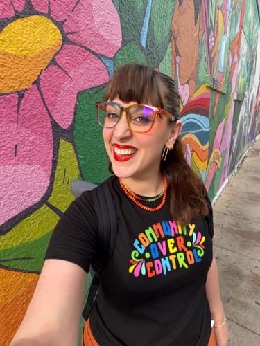 Reviewer smiling in their black Community Over Control Tee, standing before a colorful mural.