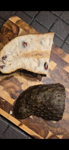 Ein Kunde zeigt eine aufgeschnittene Baby-Guanabana auf einem Holzbrett, die das cremige, weiße Fruchtfleisch enthüllt.