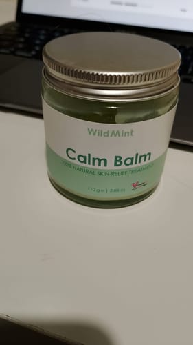 Customer's Calm Balm product in a glass jar with a silver lid, placed on a desk.