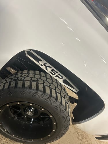 Customer's silver KSP Traction Bar Plate installed on the black wheel well liner of a white truck.