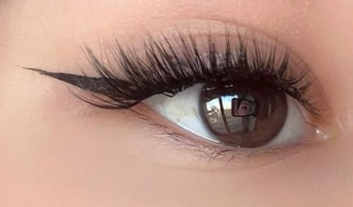 Nahaufnahme vom Auge einer Kundin, das lange Wimpernextensions zeigt, die mit dem DUO PEN BOND & SEAL befestigt wurden.