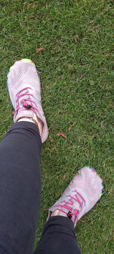 Customer wearing light-colored Smart II - Barefoot Shoes with pink laces and colorful soles on grass.