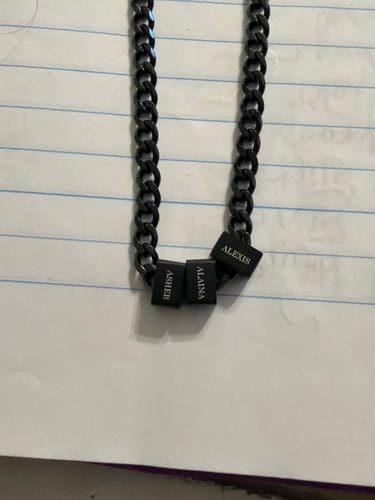 Customer's black Legacy necklace with three personalized beads engraved with 'Asher', 'Alaina', and 'Alexis' on lined paper.