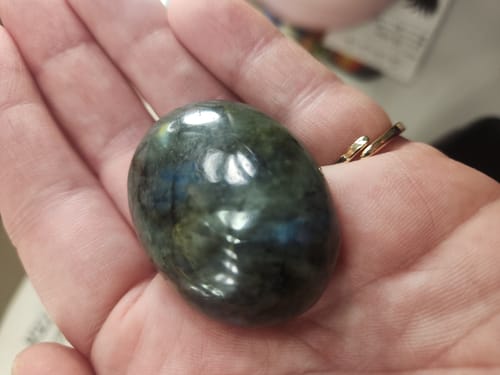 Customer's hand holding the polished, iridescent labradorite crystal from the Crystal Comfort Card Deck.