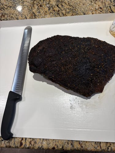 Customer's whole cooked USDA Prime Brisket with a dark bark, resting on a tray next to a large carving knife.