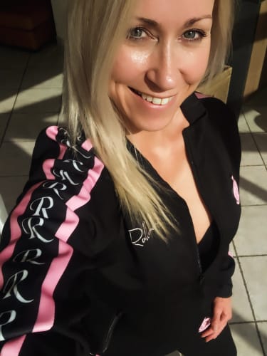 Een klant die een selfie neemt in haar zwarte ROLLEMAN trainingspak met roze en witte logodetails op de mouwen.