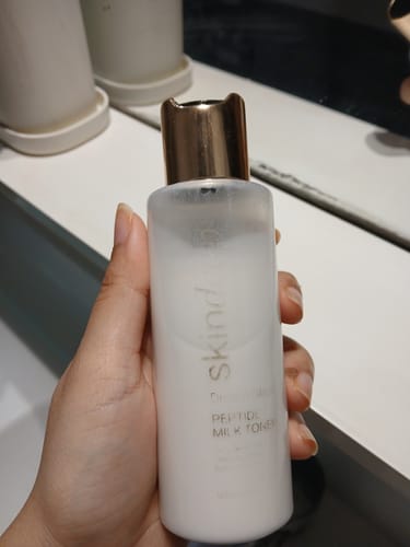 Customer holding a translucent bottle of DREAM GLAZE Peptide Milk Toner against a plain background.