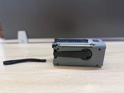 Customer's grey emergency weather radio on a table, showing the side with the folded hand crank and top solar panel.
