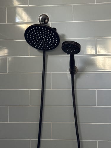 Customer's dual shower head set with a dark finish installed on a tiled wall, showing the separate handheld mount.