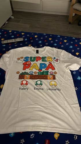 Ein Rezensent zeigt das personalisierte weiße „Super Papà“-T-Shirt mit einer bunten Grafik und Namen.