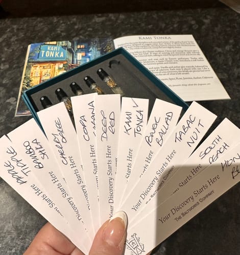 Reviewer's hand holding fanned-out, handwritten scent strips for the Limited Edition Discovery Set.
