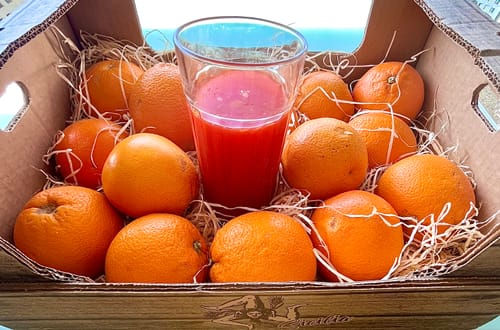 Kundenbild von Bio Tarocco Blutorangen in einer Kiste, mit einem Glas frisch gepresstem, rotem Saft.