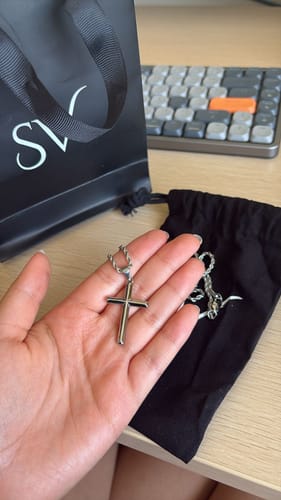 Cliente sosteniendo el colgante Crucifijo en la palma de la mano, con la bolsa de regalo y la funda de tela detrás.