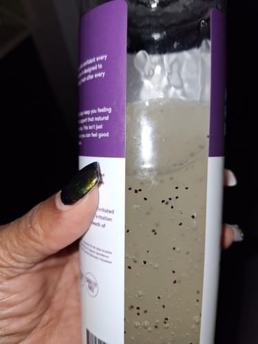 Close-up of a reviewer's hand holding a bottle of body cleanser, showing the liquid's texture with dark specks inside.