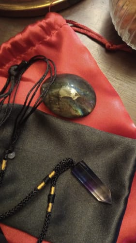 Reviewer's monthly crystal delivery showing an iridescent stone and a pointed crystal necklace with their pouches.