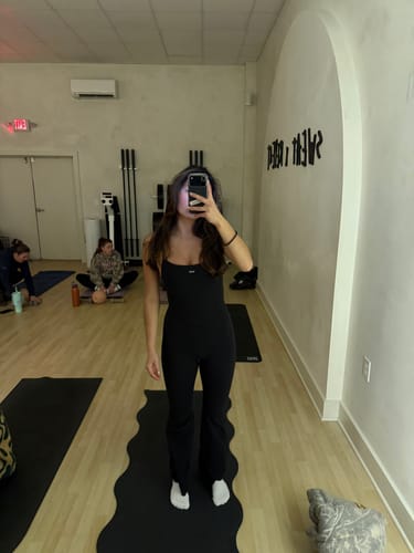 Reviewer in a studio showing the fit of the full-length black Flare Onesie.