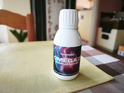 Reviewer's bottle of Omega 3 Premium Fish Oil sitting on a yellow placemat on a table.
