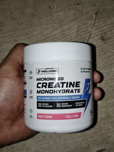 Reviewer holding a white tub of Wellcore Micronised Creatine Monohydrate in Fruit Fusion flavor.