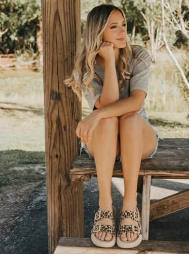 Customer wearing the leopard print Vibe platform sandals while sitting on a wooden bench outdoors.