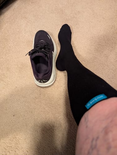 Reviewer wearing the black Performance Eucalyptus Compression Socks on their leg, seen next to a dark sneaker on the floor.