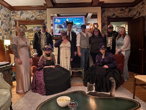 Customers posing in festive costumes and masks for their Masquerade Ball Murder Mystery game in a living room.