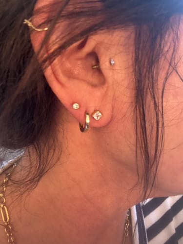 Close-up of a customer wearing the Asscher Solitaire Studs stacked with other gold earrings on their earlobe.