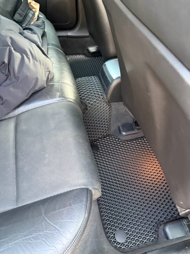 Recenzent pokazuje czarne, dopasowane dywaniki samochodowe zainstalowane na tylnej podłodze samochodu.