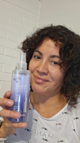 Clienta con cabello rizado sosteniendo el Spray Bifásico 10 en 1.