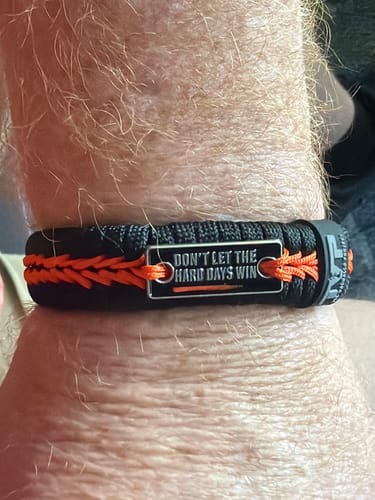 Customer wearing the black and orange Hard Days Paracord Bracelet, with the "Don't Let The Hard Days Win" plate visible.