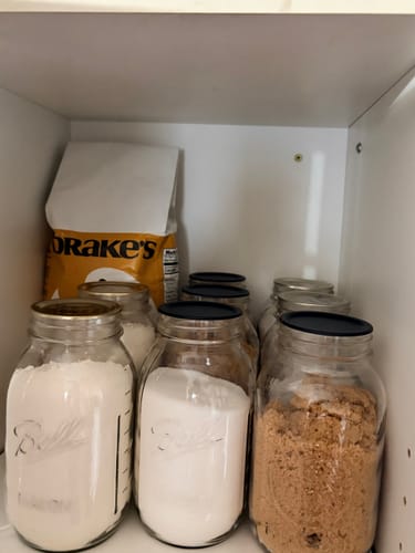 Customer's pantry shelf with several glass mason jars filled with dry goods like flour and sugar, sealed for freshness.