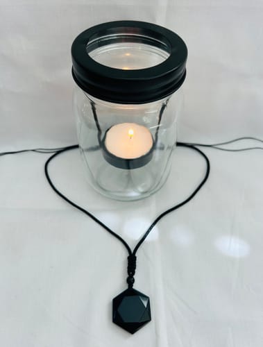 Customer's Obsidian Self Protection Necklace with its black cord shaped like a heart in front of a lit candle.