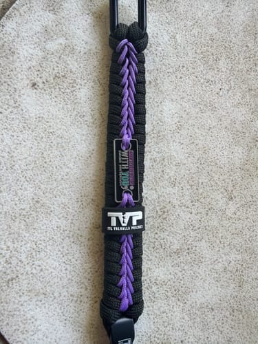 Close-up of a reviewer's black and purple 'You Belong Here' paracord bracelet, showing the TVP brand tag.