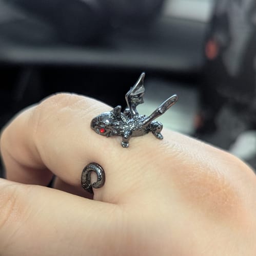 A reviewer's hand wearing the adjustable Perching Baby Dragons Ring in black, showing its detailed wings and brilliant red eye.