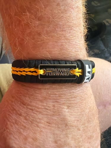 A reviewer shows their Keep Moving Forward Paracord Bracelet, featuring black and yellow braids and a metal plate.