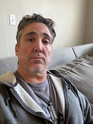 Reviewer wearing the Lord’s Prayer Crown of Thorns Necklace. The solid, rectangular cross pendant is worn over a grey shirt.