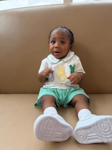Customer's child sitting down while wearing the Peeps Green Gingham Collared Short Set.