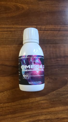 Customer's bottle of Omega 3 Premium Fish Oil with a colorful label, shown on a wooden table.