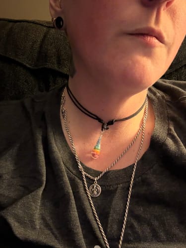 Reviewer wearing the colorful Dainty Rainbow Drop Pendant on a black cord, layered with other necklaces.