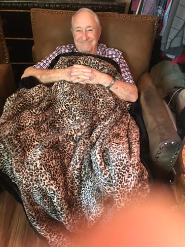 Customer smiling while relaxing in a chair, covered by a plush, leopard-print minky blanket.