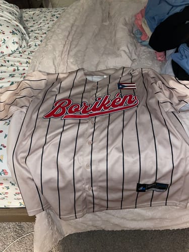 Customer's pinstriped Puerto Rico Heritage Baseball Jersey laid on a bed, showing the front with 'Borikén' in red script.