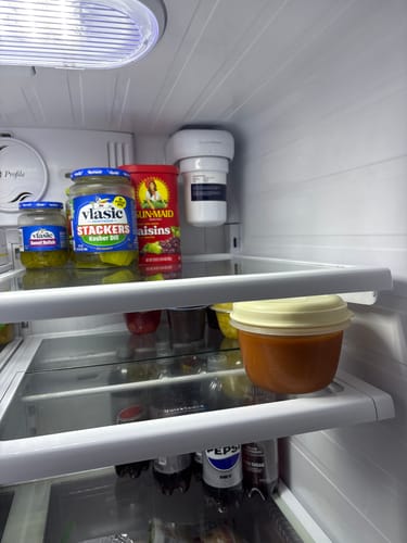 Customer's white replacement water filter installed in the top corner of their refrigerator, next to food items.