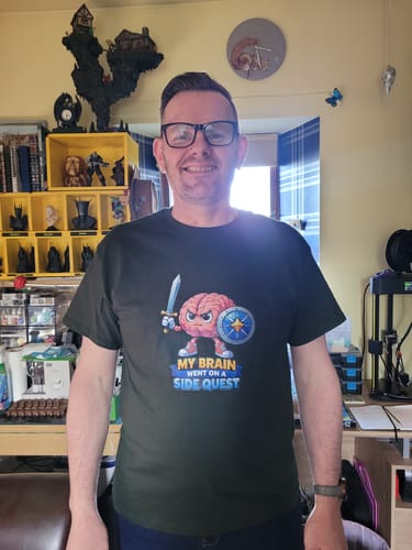 Reviewer smiling in a dark unisex t-shirt featuring a cartoon brain with a sword and 'My Brain Went On A Side Quest' text.