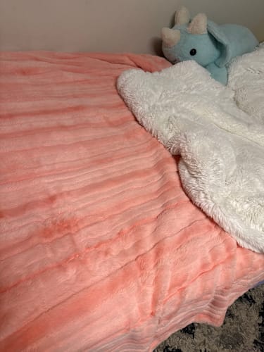 Customer's pink, textured Blossom Vienna Blanket spread on a bed with its white fluffy side showing.