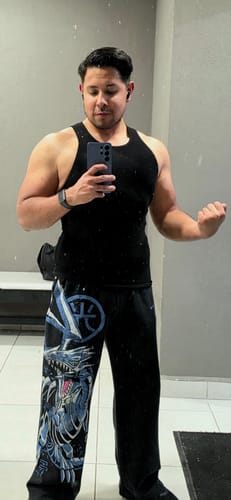 Reviewer at the gym flexing in a fitted black 340 Wife Lovers tank top, taking a mirror selfie.