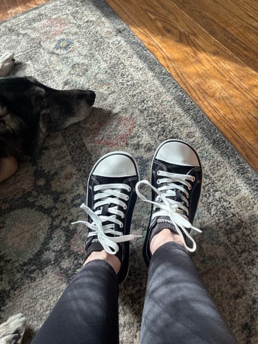 Reviewer's point-of-view of their feet wearing the black canvas Roam I - Barefoot Shoes indoors.