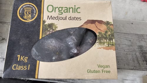 Rezensent zeigt die Verpackung der Bio-Medjool-Datteln auf einem Holztisch.